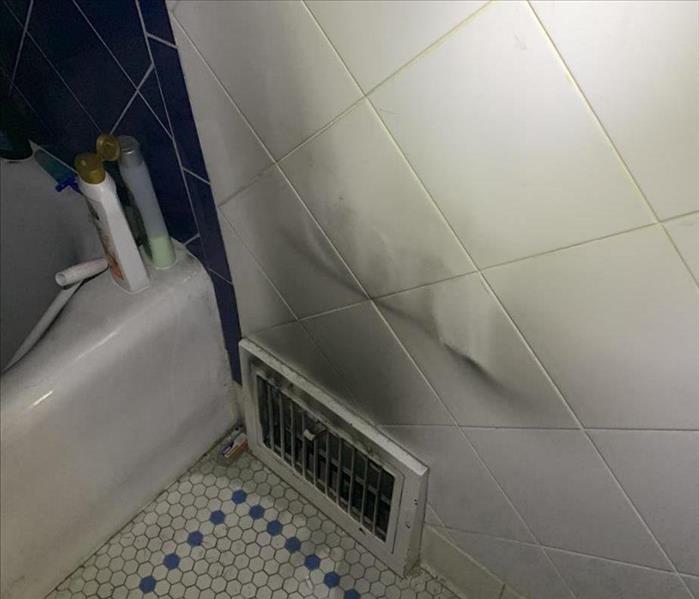 Bathroom wall heat register with black soot surrounding it