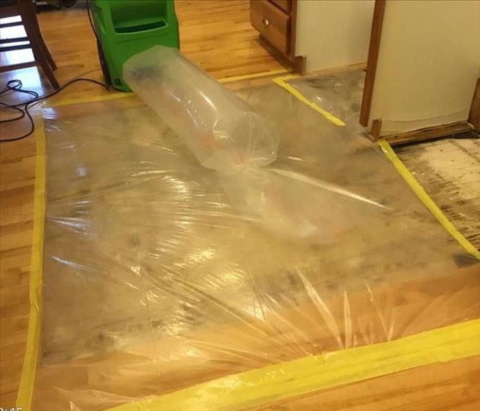Clear plastic taped over a section of flooring where the hardwood floor has been removed and warm air is forced in