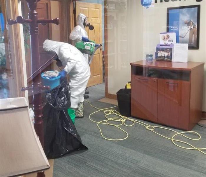 Two people wearing full personal protective equipment working in an office