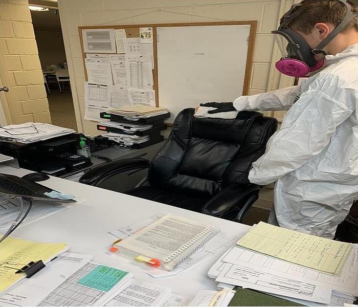 A SERVPRO employee is in PPE cleaning a desk area for COVID contamination 