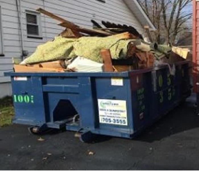 A dumpster is in a driveway and is very full
