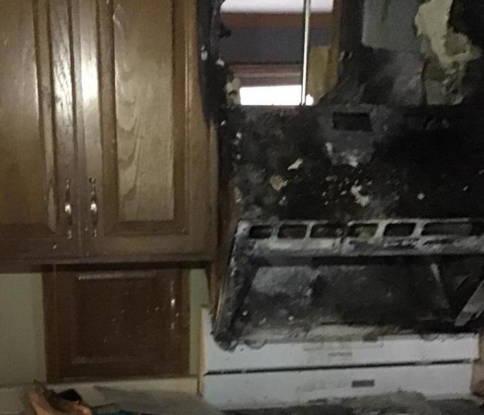 Kitchen cabinets next to a black, charred microwave and stove