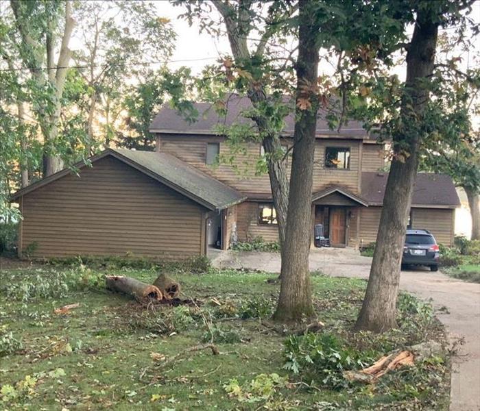 Front of home with tree limbs broken off and leaves laying on the ground all over the property