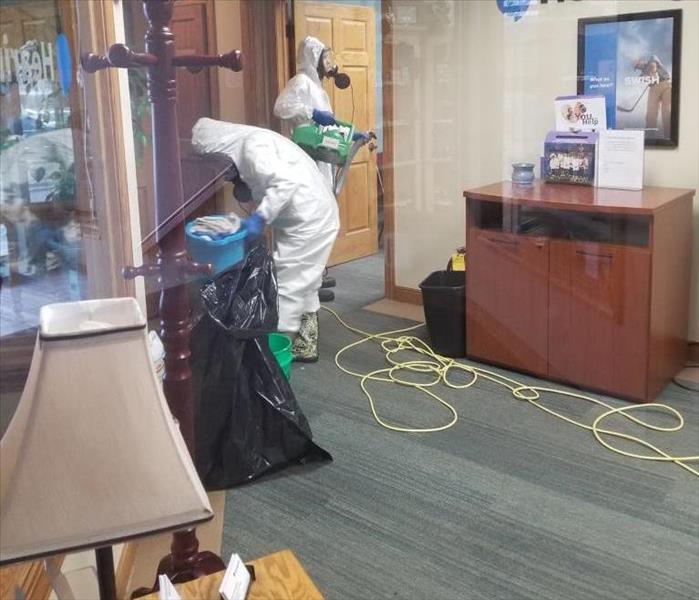 Two people wearing personal protective equipment cleaning in a reception area