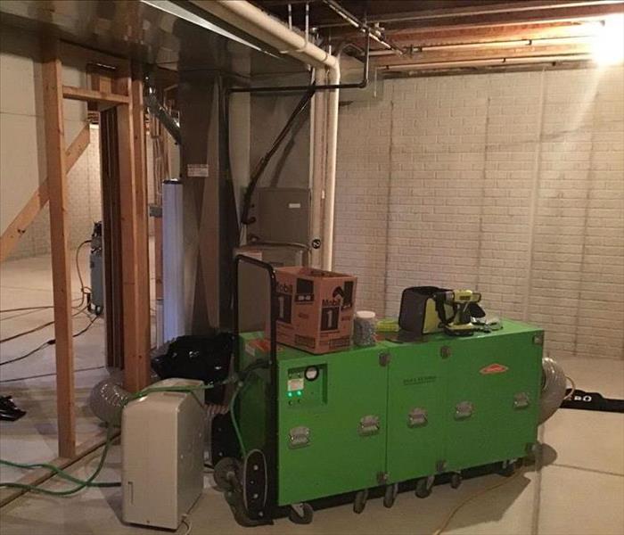 A green machine sits on a basement floor and is connected to a furnace