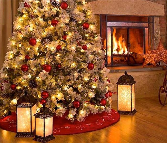 Decorated Christmas tree with lights on resting near a fire place with flames and sitting next to candles