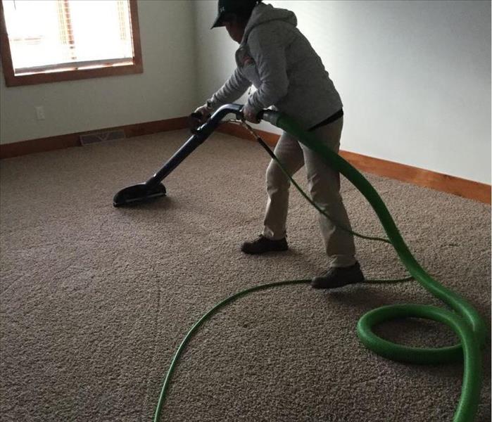 Person with hose connected to carpet wand removing water from the carpet