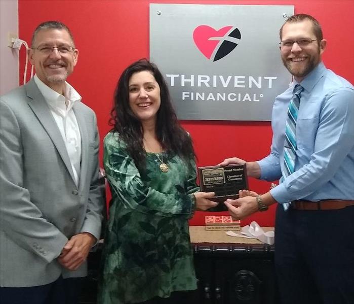 Female presenting a plaque to two males with a Thrivent Financial sign hanging on the wall behind them