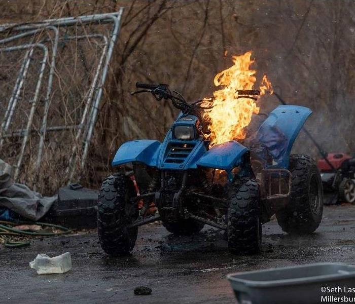 Blue ATV on fire in a yard
